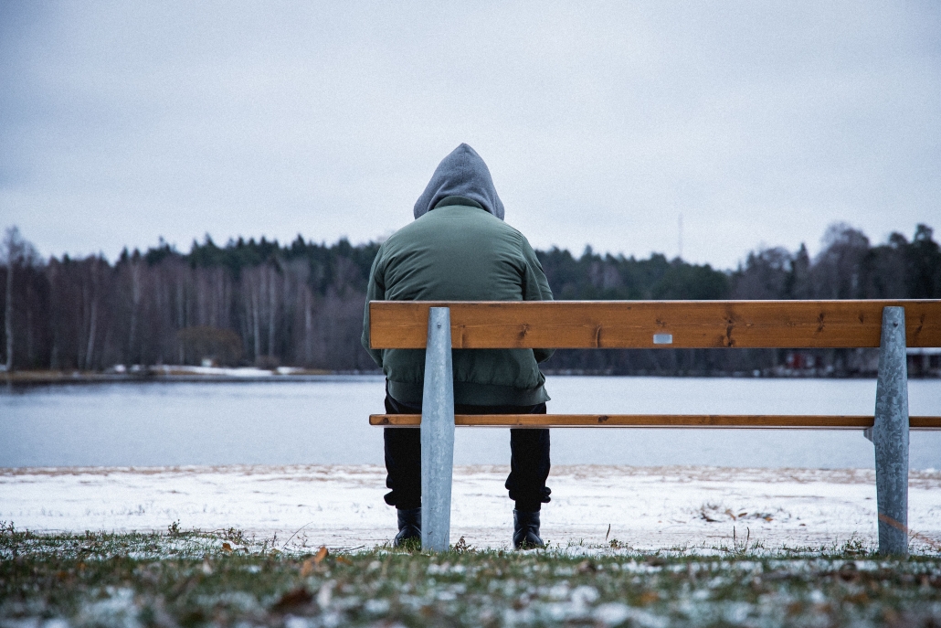 Lonely man sitting on the bench in a snowy park